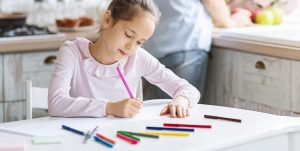 Pretty little girl busy with drawing at kitchen table